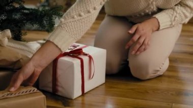 Kafkasyalı genç bir kadın Noel ağacının altına Noel hediyesi koyuyor. 8K 'da kırmızı helyum kamerayla çekildi..   
