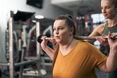 Beyaz kadınlar spor salonunda kanepede ağırlık kaldırıyor.