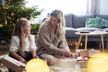 Beyaz bir kız ve anne yerde Noel hediyelerini paketliyor. 