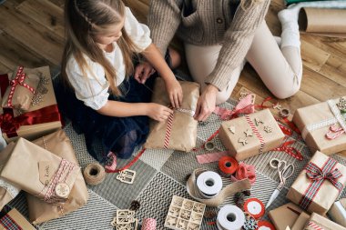 Beyaz bir kız ve annenin Noel hediyelerini yere sarmaladığı yüksek açılı manzara. 