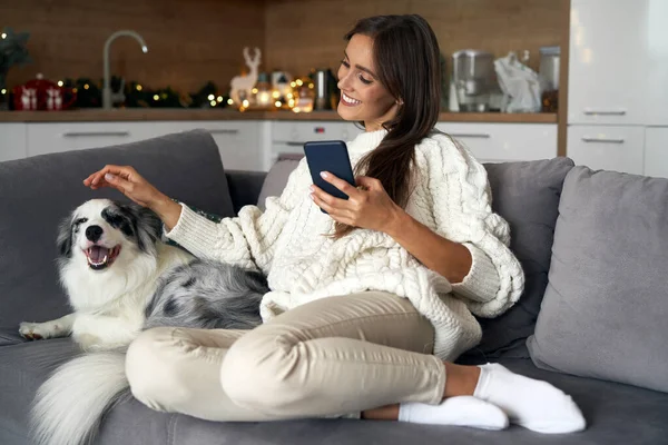 Mulher Com Cachorro Refrigerando Sofá Com Telefone Celular Durante Natal — Fotografia de Stock