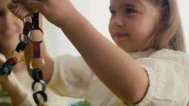 Kafkas küçük kız ve annesinin Noel ağacını boyanmış kağıt zincir ile süslemesine yakın durun. 8K 'da kırmızı helyum kamerayla çekildi..  
