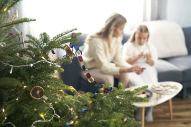 Ön planda Noel ağacı ve dekorasyon yapan kızı beyaz bir kadın. 