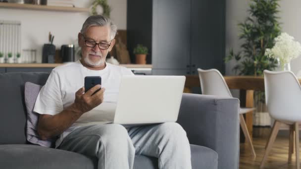 Senior Kaukasische Man Zit Bank Gebruikt Laptop Met Mobiele Telefoon — Stockvideo