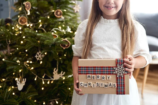 クリスマスツリーの横に立っている間 白人の女の子はクリスマスプレゼントを保持 — ストック写真