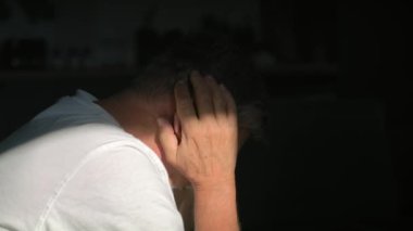 Zihinsel sorunları olan kıdemli beyaz adam karanlıkta oturuyor. 8K 'da kırmızı helyum kamerayla çekildi..  