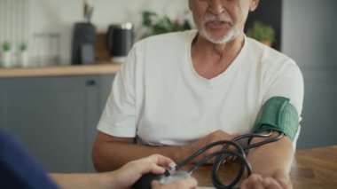 Beyaz kadın doktor, yaşlı adamın ev ziyaretindeki baskısını ölçüyor. 8K 'da kırmızı helyum kamerayla çekildi..  