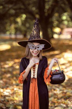 Büyücü kıyafetli ve ormanda dikilen kızın dikey görüntüsü.