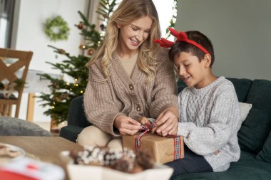 Beyaz çocuk ve anne kanepeye Noel hediyesi koyuyorlar. 