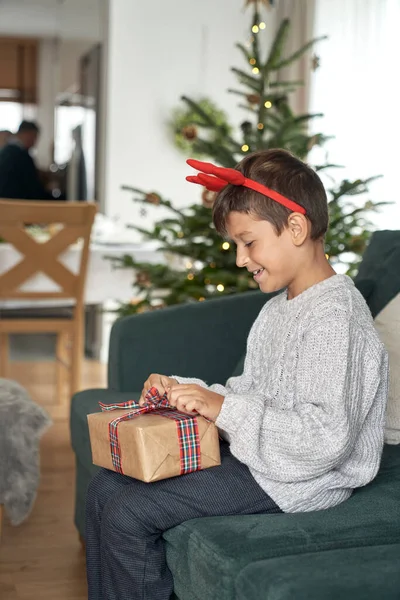 Kaukázusi Fiú Készül Kinyitni Karácsonyi Ajándék Miközben Kanapén — Stock Fotó