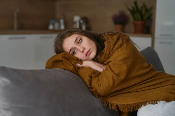 Caucasian terrified woman lying on the sofa under the blanket