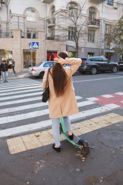 Şehrin göbeğinde karşıdan karşıya geçen elektrikli scooterlı bir kadının görüntüsü.