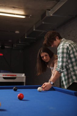 Genç bir adamın kız arkadaşına bilardo öğretirken çekilmiş dikey görüntüsü.