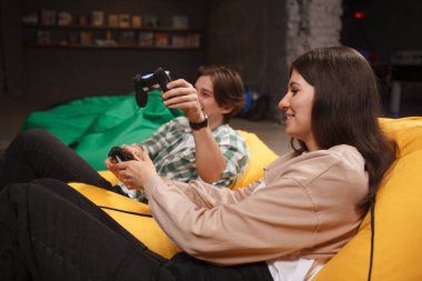 Genç, güzel bir kadın gülümsüyor, erkek arkadaşıyla video oyunları oynuyor.