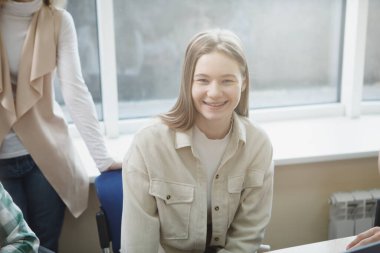 Çekici genç bir üniversite öğrencisi gülümsüyor, sınıfta oturuyor.