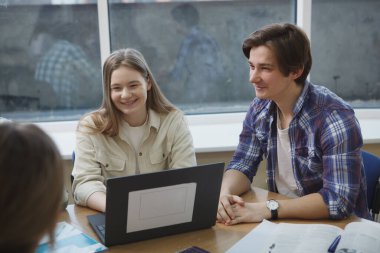 Neşeli üniversite öğrencileri gülümsüyor, sınıfta bir proje üzerinde çalışmaktan keyif alıyorlar.