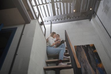 Bir anne ve oğlunun çatı katındaki merdivenlerde oturduğu düşük açılı, uzun açılı bir çekim.