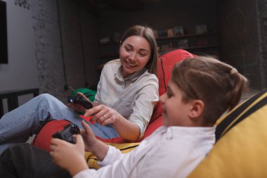 Genç çocuk eğleniyor, annesiyle video oyunu oynuyor.