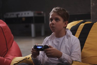 Video oyunu oynarken, elinde parlak bir konsol tutarak komik surat ifadesi takınan sevimli çocuk.