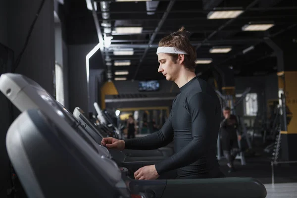 Young sportsman wearing headband, walking on a treadmill at the gym