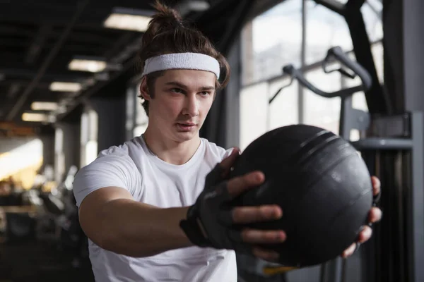Male athlete wearing headband, looking focused, exercising with medicine ball