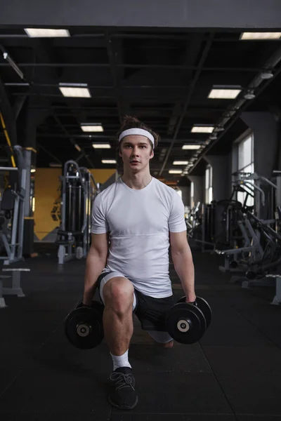 Vertical full length shot of a male athlete doing lunges with dumbbells