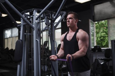 Muscular sportsman warming up at the gym, doing biceps curls with resistance band