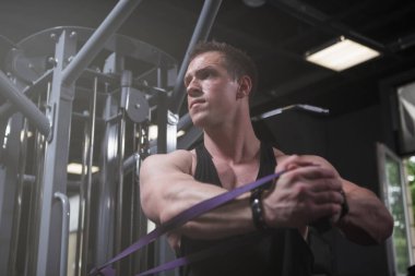 Focused muscular man training with resistance rubber band at the gym, copy space