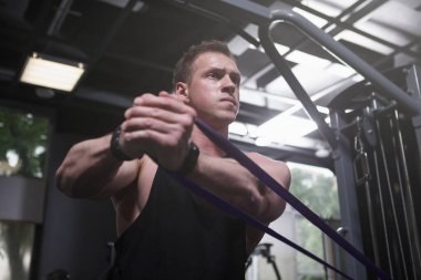 Focused male bodybuilder doing resistance band workout at the gym