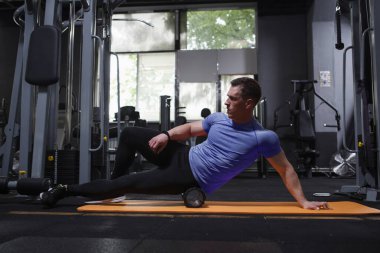 Professional athlete stretching muscles, using foam roller at the gym