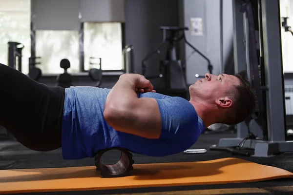 Male athlete using foam roller, relaxing back muscles after exercising at the gym