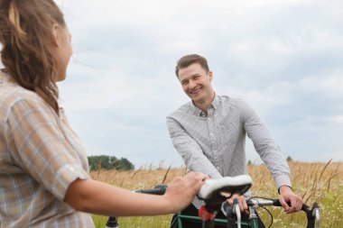Mutlu çift tarlanın yakınında bisiklet sürüyor. Bisikletli bir adam ve bisikletli bir kadın yazın tarlaların yakınına gidiyorlar..