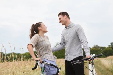 Mutlu çift tarlanın yakınında bisiklet sürüyor. Bisikletli bir adam ve bisikletli bir kadın yazın tarlaların yakınına gidiyorlar..