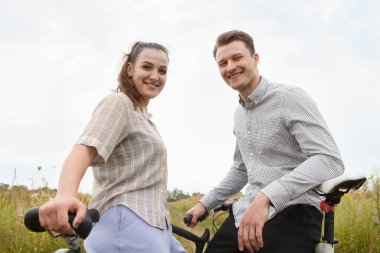 Mutlu çift tarlanın yakınında bisiklet sürüyor. Bisikletli bir adam ve bisikletli bir kadın yazın tarlaların yakınına gidiyorlar..