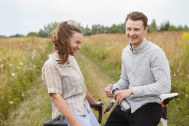Mutlu çift tarlanın yakınında bisiklet sürüyor. Bisikletli bir adam ve bisikletli bir kadın yazın tarlaların yakınına gidiyorlar..