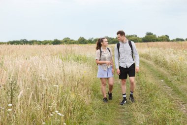 Çim eniyim yolunda yürürken aşık genç çiftin açık hava fotoğrafı. Uzun ot tarlasında yürüyen erkek ve kadın.