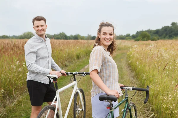 The happy couple cycling near the field. Cyclists man and a woman with bicycles go near the fields  in summer.