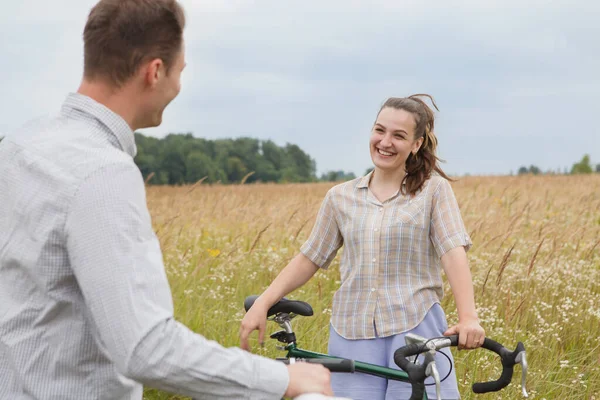 The happy couple cycling near the field. Cyclists man and a woman with bicycles go near the fields  in summer.