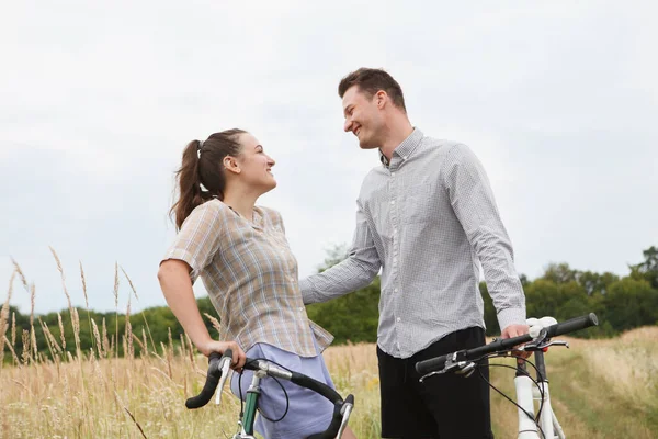 The happy couple cycling near the field. Cyclists man and a woman with bicycles go near the fields  in summer.