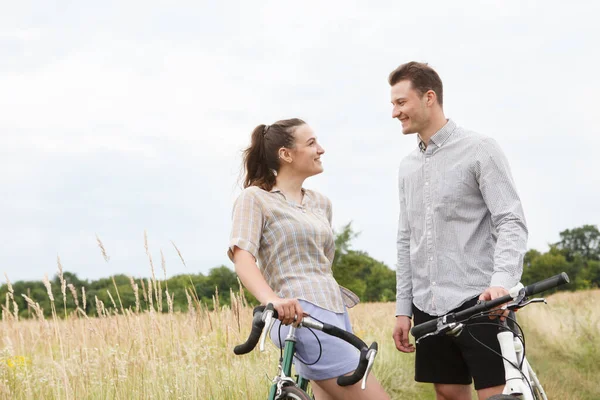 The happy couple cycling near the field. Cyclists man and a woman with bicycles go near the fields  in summer.