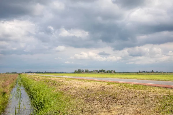 The bank of a creek, typical landscape of Holland, flat land and water and a blue sky with white clouds, horizon over land