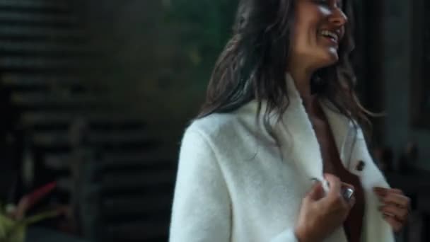 Mladá a krásná evropská dívka dlouhosrstá brunetka doma v podzimním oblečení a bílý svetr a usmívající se pohledy do kamery dotýkající se oblečení