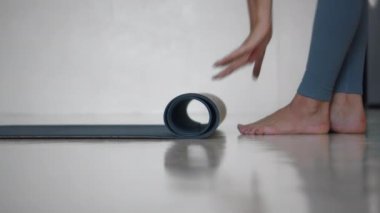 Genç Avrupalı bir kız evdeki parlak beyaz bir odada yoga minderini boyluyor. Evde tek başına spor yap..