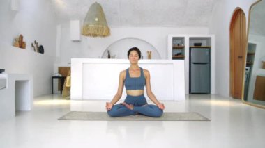 Çekici Avrupalı genç esmer kız yoga yapmak için halının üzerinde beyaz parlak bir odada yoga yapıyor. Evde tek başına spor yap..