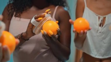 Avrupalı, Asyalı ve Afrikalı genç kızlar banyoda eğleniyor ve portakalların derisi cilt temizleme tezgahıyla korkakça eğleniyor.