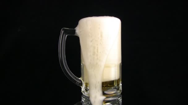 La espuma de cerveza se vierte a través del borde de la taza. Fondo negro — Vídeos de Stock