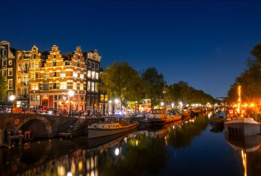 Hollanda 'da. Amsterdam 'ın gece kanalı sakin olsun. Mavnalar ve tekneler demirli. Geleneksel evlerin sularında yansıma ve bir köprü