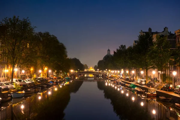 Netherlands. Night Amsterdam. Many boats are moored along the banks of the canal. Lanterns and parked cars on the embankments