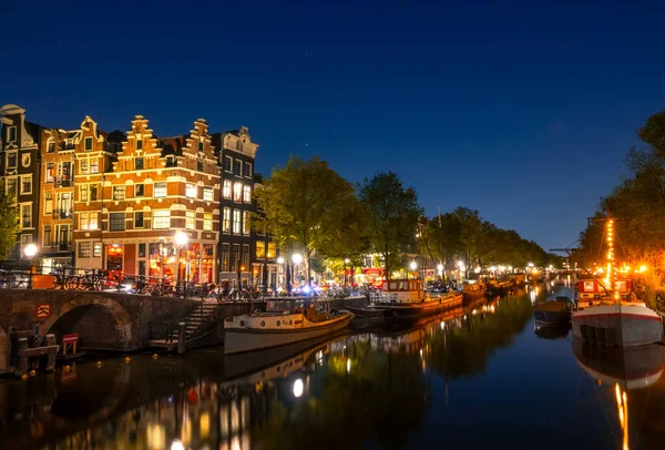Hollanda 'da. Amsterdam 'ın gece kanalı sakin olsun. Mavnalar ve tekneler demirli. Geleneksel evlerin sularında yansıma ve bir köprü