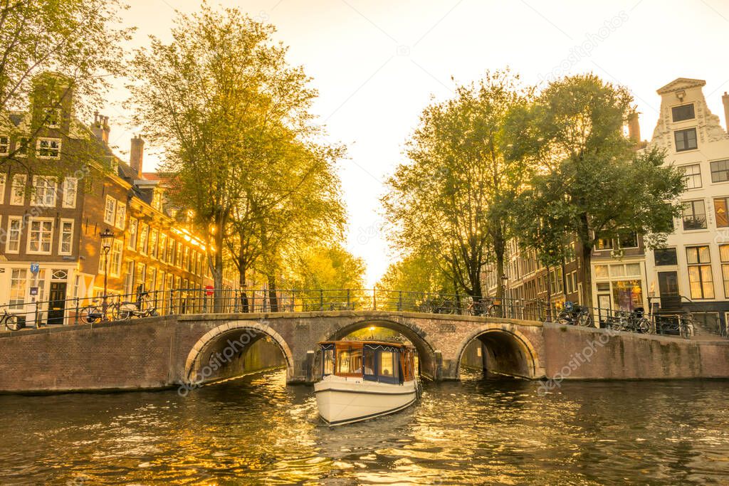 Autumn evening on the Amsterdam Canal. The boat will come out from under the bridge. Typical houses and many bicycles on the waterfront